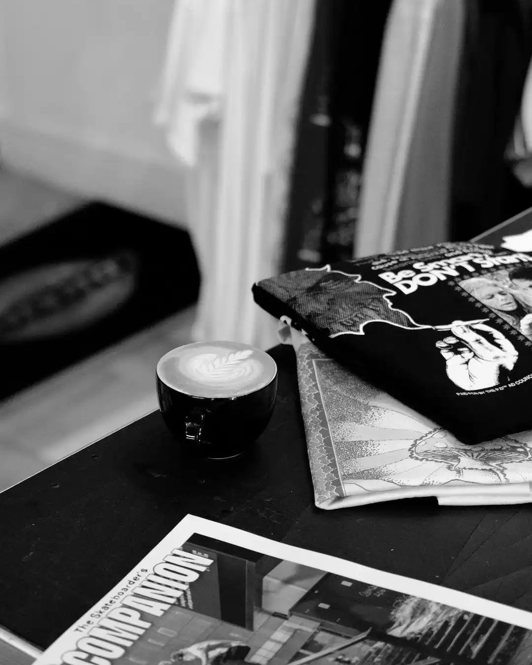 A cup of coffee with a heart-shaped latte art pattern sits beside some magazines.