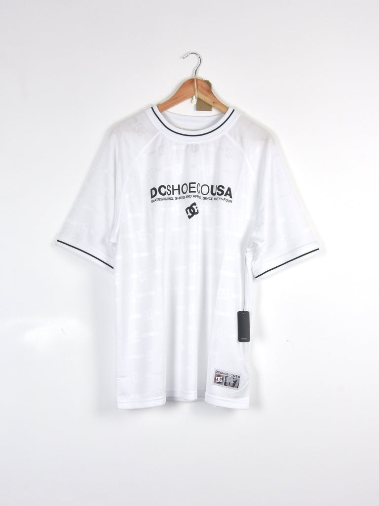 White t-shirt with ’DC SHOES USA’ text and black trim hanging on a wooden hanger.