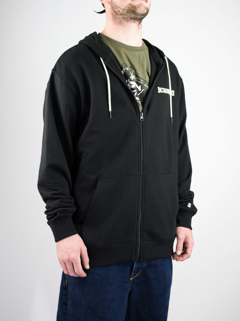 Black zip-up hooded sweatshirt with a logo worn over a green t-shirt.