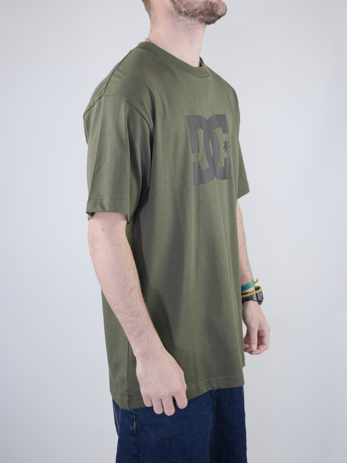 Olive green t-shirt with a dark DC logo graphic on the front.