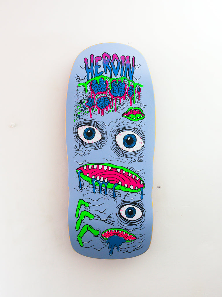 Light blue skateboard deck featuring cartoon-style monster faces with multiple eyes and mouths in neon green and pink colors.