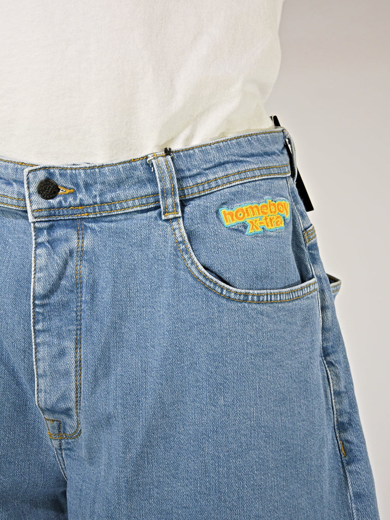 Light blue denim jeans featuring a yellow Homeboy logo patch, part of Homeboy Xtra Monster collection