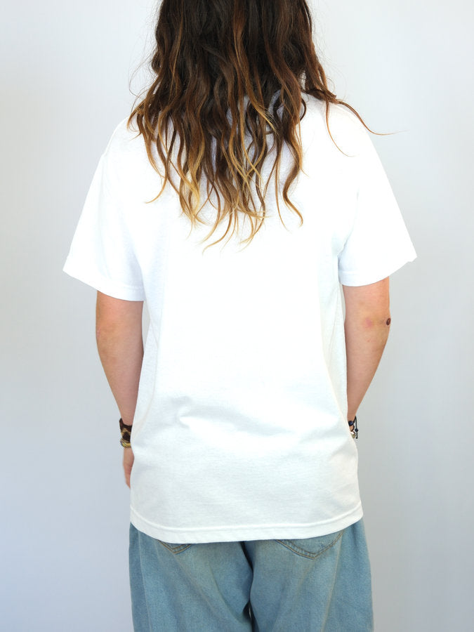 Person with long wavy brown hair wearing Snack Skateboards Blackbird Tee Shirt in white