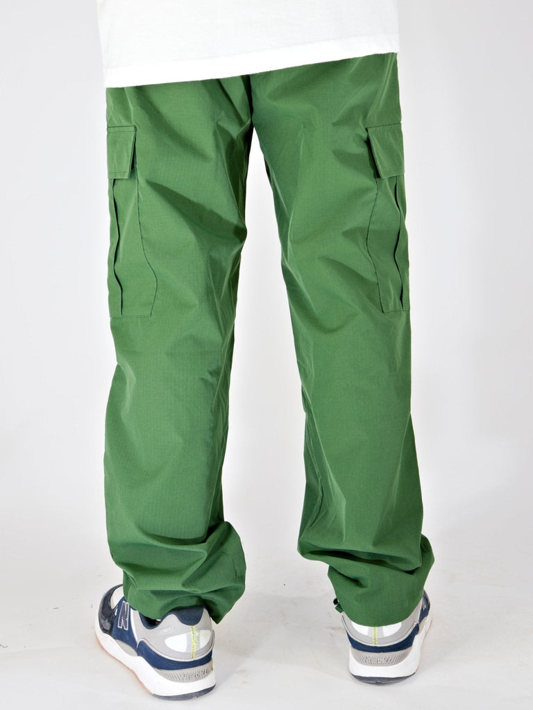 Green Ninja Cargo Pants with side pockets, worn over sneakers, by Snack Skateboards