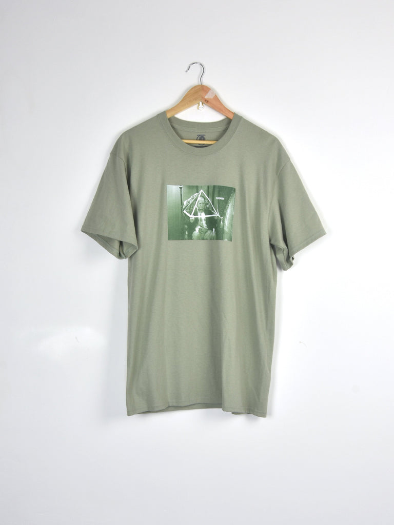 Sage green t-shirt with a square graphic design hanging on a clothes hanger.