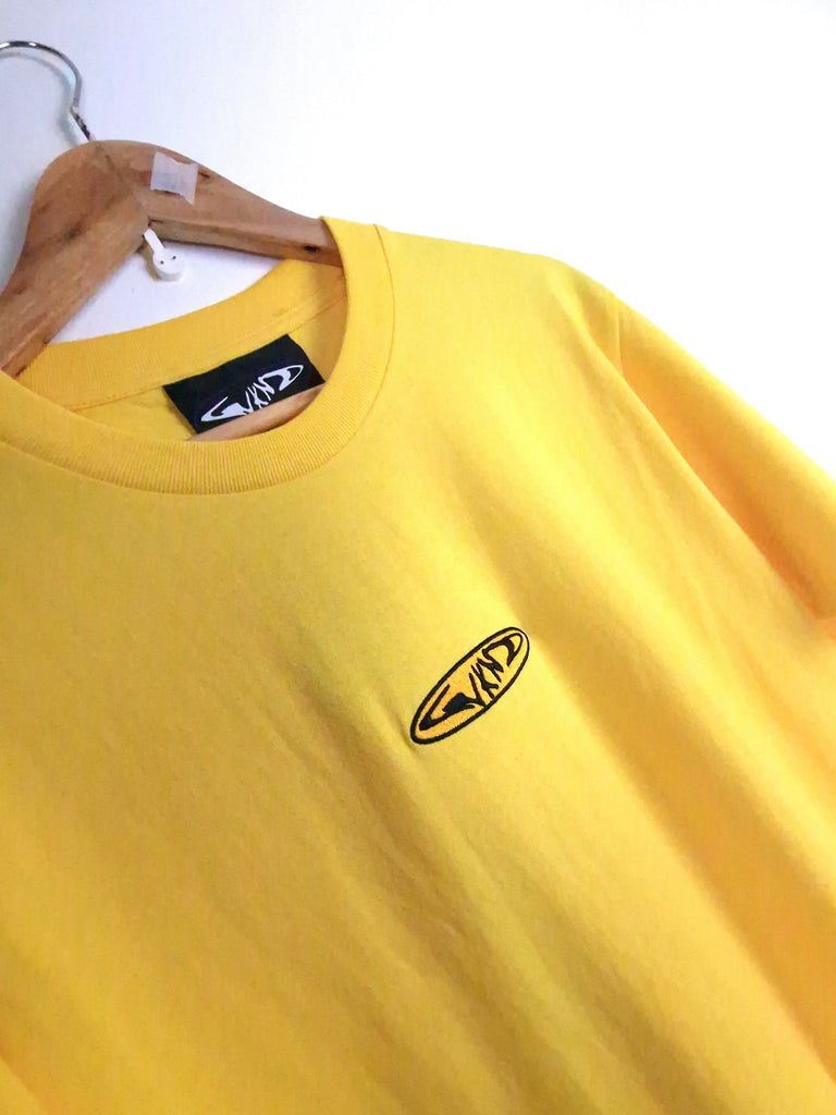 Yellow t-shirt with an oval logo on a wooden hanger.